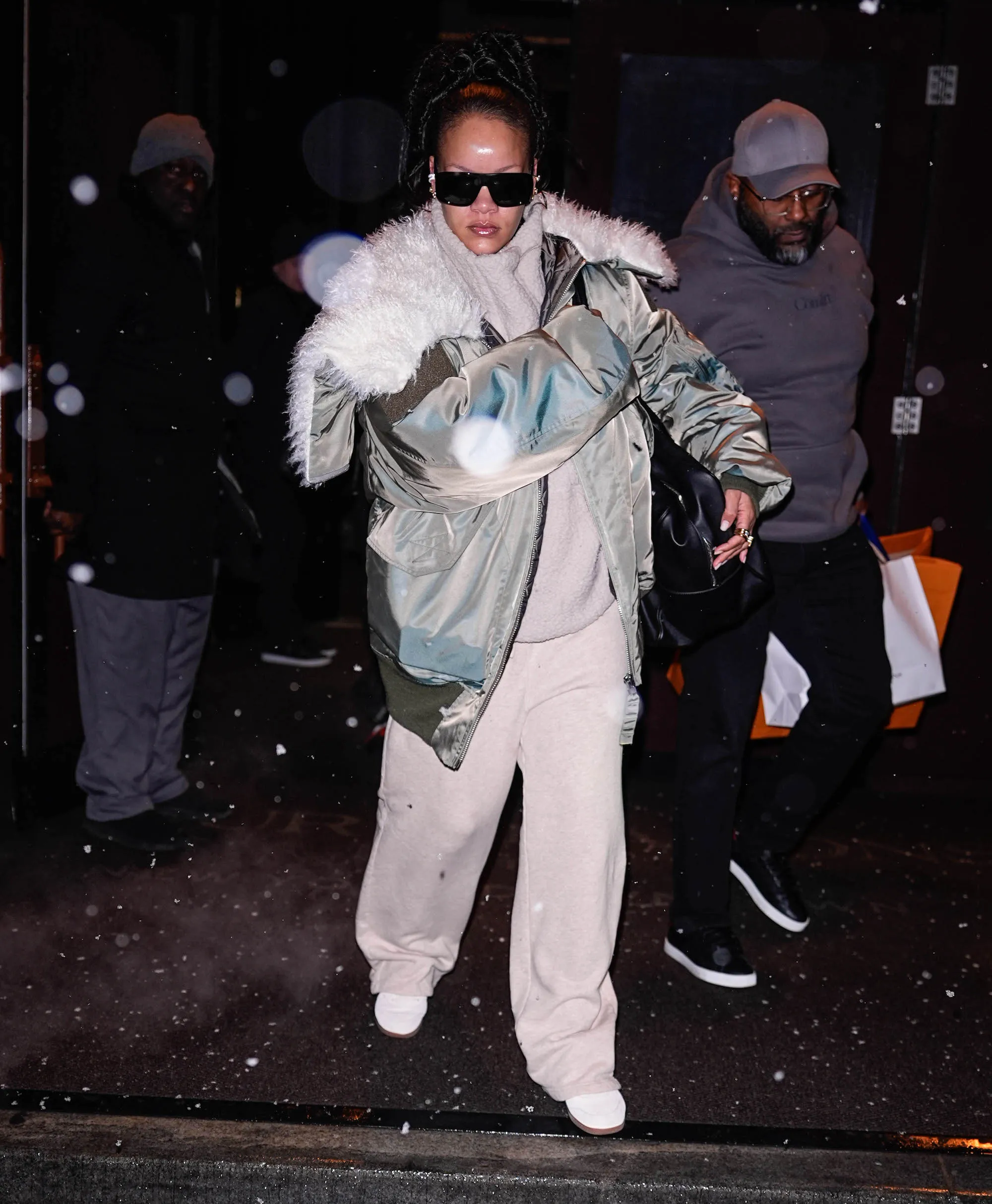 Rihanna walking in NYC snow wearing a sage green Vaquera aviator jacket, cream sweatpants, and white PUMA sneakers.